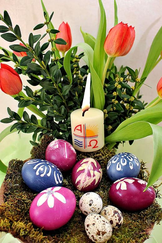gefärbte Eier in einer Schale, brennende Osterkerze, rote Tulpen mit Buchs