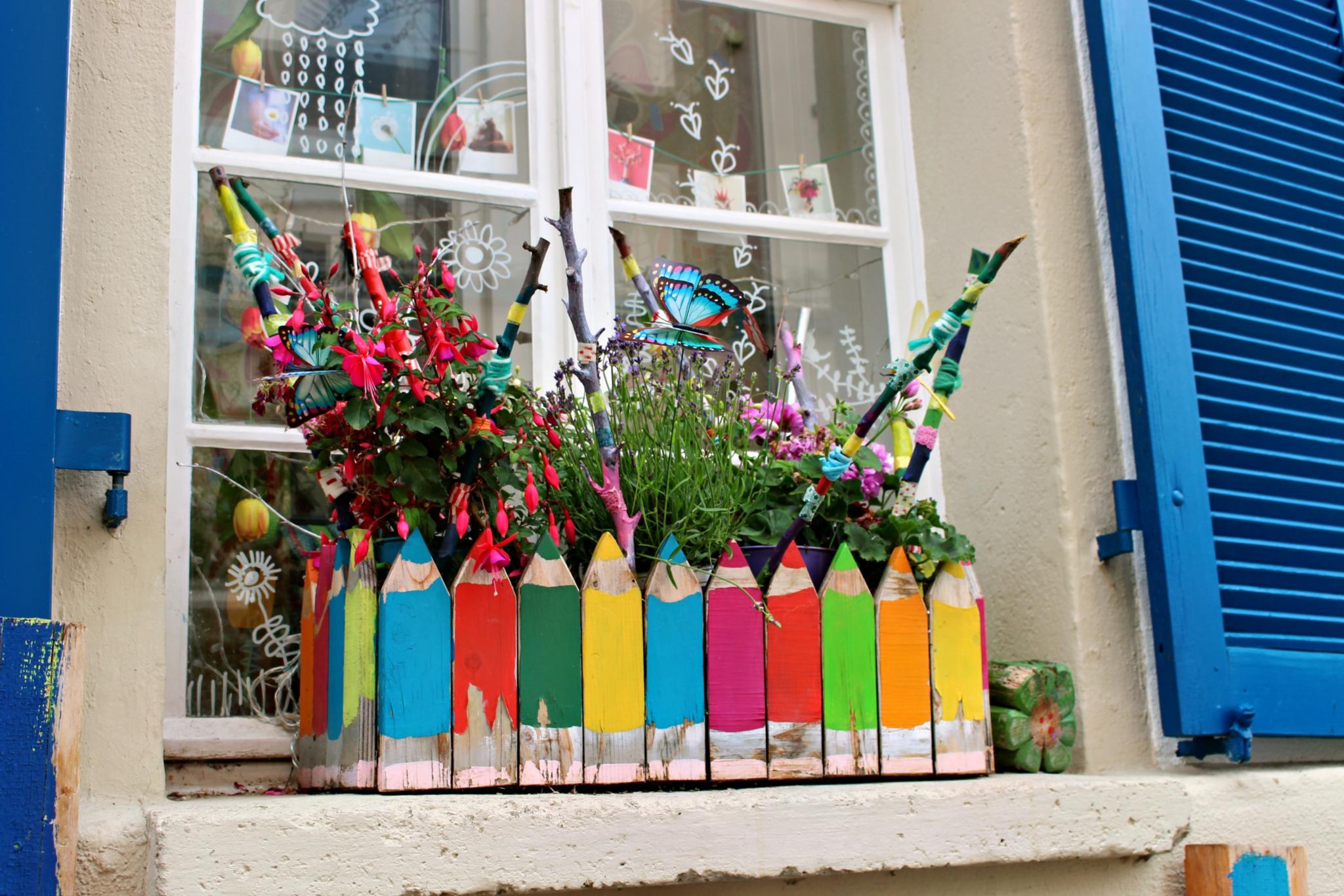 Ein Blumenkasten mit einem Zaun. Die Zaunlatten sind in Form und Farbr von Stiften.