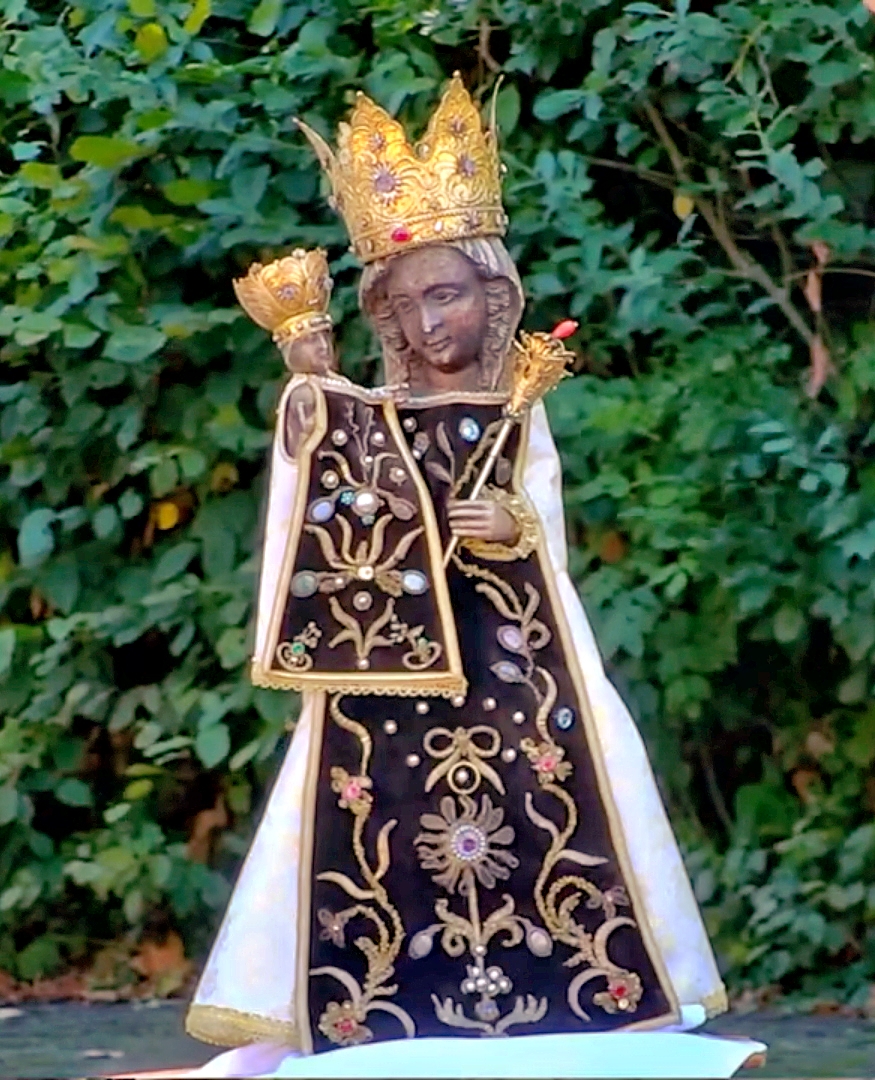 schwarze Madonna vor einer grünen Hecke
