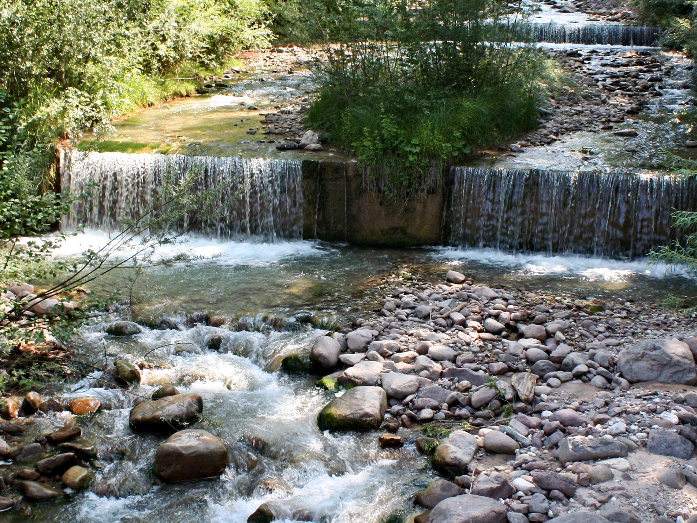 Bachlauf mit kleinen Wasserfällen. Das Wasser fällt wie ein breiter Vorhang